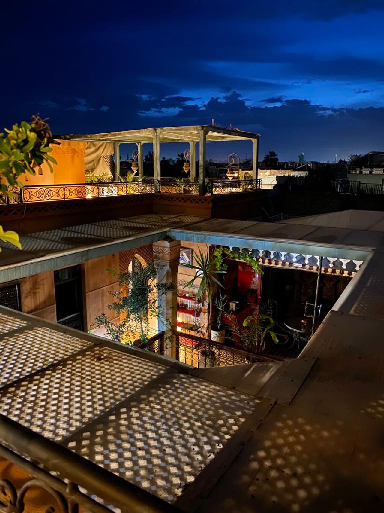 La terrasse d’un riad de Marrakech à la tombée de la nuit, avec son patio éclairé et une pergola sur le toit